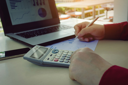 hand working with finances about cost and calculator, business strategy diagram report and laptop computer on desk at home office, income and expenses, plan money cost savings and business conceptの写真素材