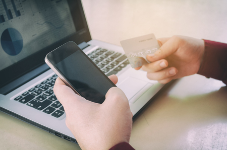 hand paying with credit card and using smart phone with business strategy diagram report in laptop screen on desk at home office, payment and shopping online, income and expenses and economy conceptの写真素材