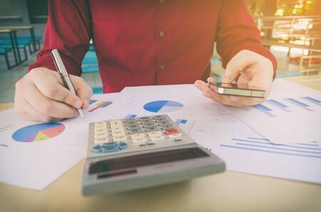 hand working writing and using smart phone with business strategy diagram report, calculator on desk at home office, income and expenses, finance, searching data, money cost savings, economy conceptの写真素材
