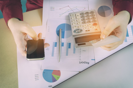 top view young man entering security code with smart phone and paying with credit card and business strategy diagram report, laptop on desk at home office, expenses, payment, shopping online conceptの写真素材
