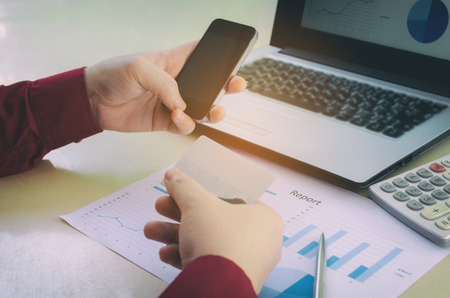 young man entering security code with smart phone and paying with credit card and business strategy diagram report, laptop computer on desk at home office, expenses, payment, shopping online conceptの写真素材