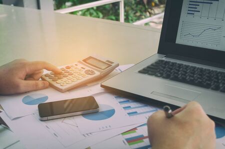 hand working and analyzing business strategy diagram report, graph and chart document with calculator and laptop computer on desk at home office, income and expenses, finance and economy conceptの写真素材