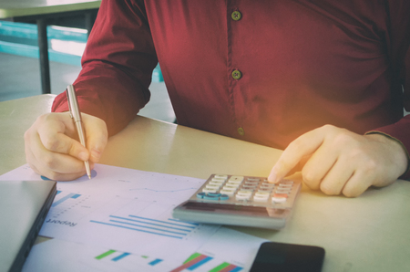young business man writing, working and analyzing business strategy diagram report, graph and chart document with calculator on desk at home office, income and expenses, finance and economy conceptの写真素材