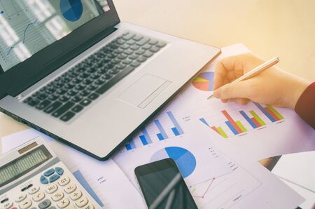 hand working and analyzing business strategy diagram report, graph and chart document with calculator and laptop computer on desk at home office, income and expenses, finance and economy conceptの写真素材