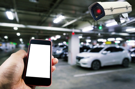 hand using smart phone monitoring and CCTV security indoor camera system operating in indoor car parking garage area, RFID solution management system, internet, security and safety technology conceptの写真素材