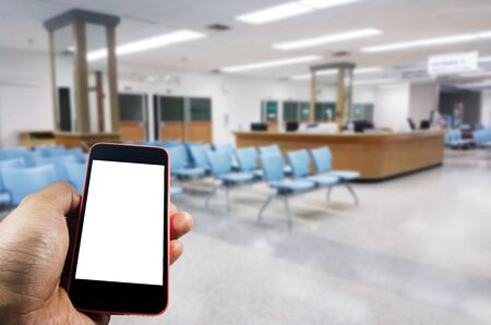 hand using smart phone with blurred image of empty chairs in waiting room at clinic or hospital, medical, internet, network connection, searching information, social media, payment online conceptの写真素材