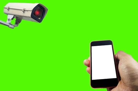 hand using smart phone with white screen monitoring and CCTV security indoor camera system operating isolated on green background for photo montage, surveillance security and safety technology conceptの写真素材