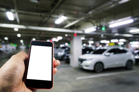 hand using mobile smart phone with blurred image of indoor car parking garage area, RFID solution management system, internet, social media and car parking sensor technology conceptの写真素材
