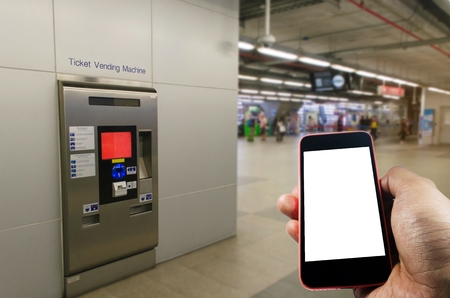 hand holding white blank screen mobile phone with self service ticket or ticket vending machine at train station, transportation, technology, internet, network connection and social media conceptの写真素材