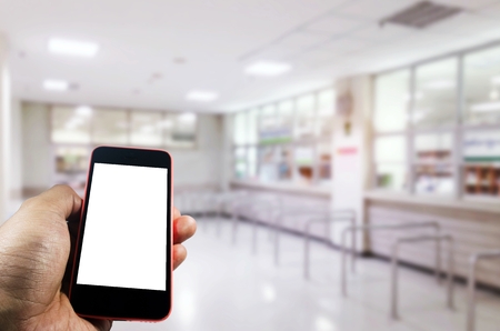 hand holding mobile phone with blurred image of waiting zone for pay money and receive medicine at cashier pharmacy counter at hospital, medical, technology, internet and social media conceptの写真素材