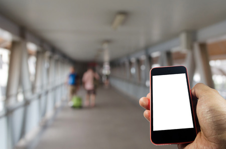 hand holding white blank screen mobile phone with blurred image of people walking with luggage at...