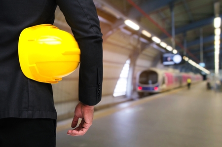 back view of engineer and holding yellow safety helmet standing in front of sky train at train station background, industrial, transportation and business conceptの写真素材