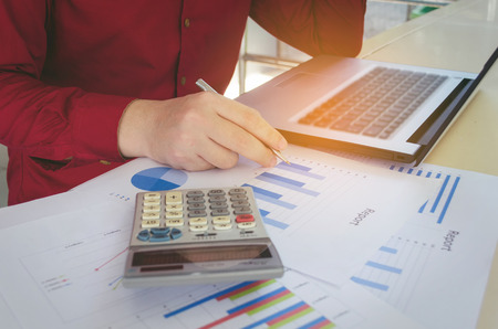 stressed young businessman hand working about cost with laptop, calculator and paper work on desk at home office, people, business, technology, finance, expenses and economy conceptの写真素材