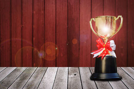 champion golden trophy with lens flare effect on wooden table and old wooden wall background, winner, success and congratulation concept, copy space for display of product presentationの写真素材