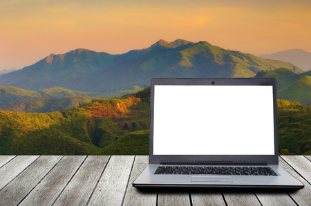 laptop computer with blank screen for presentation on wooden desk with beautiful sunset in the mountains, landscape nature background, workspace, technology, internet and business conceptの写真素材