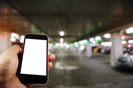 hand using mobile smart phone with blank screen for text with blurred image of intelligent car parking garage area, internet, technology and RFID solution management system concept, color tone effectの写真素材