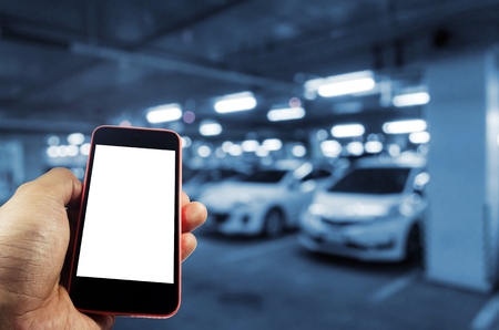 hand using mobile smart phone with blank screen for text with blurred image of underground car parking garage area background, internet, technology and searching information concept, blue color toneの写真素材