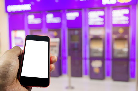 hand holding mobile phone with blank screen for e-banking with ATM banking machine at bank in background, internet, financial, payment and shopping online conceptの写真素材