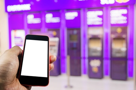 hand holding mobile phone with blank screen for e-banking with ATM banking machine at bank in background, internet, financial, payment and shopping online conceptの写真素材