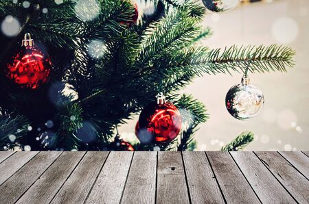 wooden terrace or desk with copy space for display of product or object presentation with decoration ball hanging on christmas tree with snow effect background, happy new year and christmas conceptの写真素材