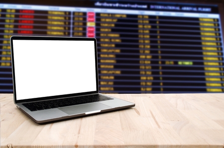 laptop notebook computer with white blank screen with blurred view of flight information timetable at international airport, flight booking online, internet technology, advertisement conceptの写真素材