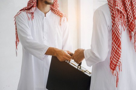 Arabian business man transfer deal after finishing up a business meeting in office, handover of a briefcase in hand of partner, successful, meeting, partner, teamwork, community, connection conceptの写真素材