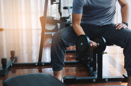 muscular asian young handsome man doing the exercises with dumbbell at biceps in fitness gym, bodybuilder, healthy lifestyle, exercise fitness, workout and sport training concept, sunlight effectの写真素材