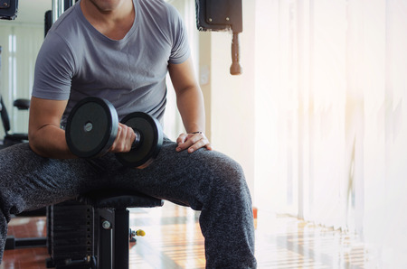 muscular asian young handsome man doing the exercises with dumbbell at biceps in fitness gym, bodybuilder, healthy lifestyle, exercise fitness, workout and sport training concept, sunlight effectの写真素材