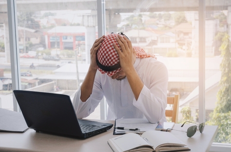 stressed young Arabian business man working finance about cost with laptop computer, mobile phone and document on desk at home office, emotion, financial, business technology and investment conceptの写真素材