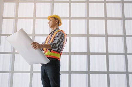 smart engineer, architect or technician with yellow safety helmet holding blueprint in construction site building to greeting start up project, successful, business, industry, construction conceptの写真素材