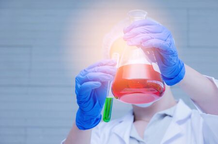young female scientist in protective mask and gloves dropping red and green liquid substance into test tube in chemical laboratory lab, science, chemistry, biology, pharmacy, medical research conceptの写真素材