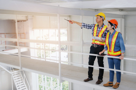 couple of engineers or technician man and woman with safety helmet holding blueprint in construction site building to greeting start up project, successful, business, industry, construction conceptの写真素材