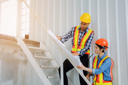 couple of engineer or technician man and woman with safety helmet looking blueprint in construction...