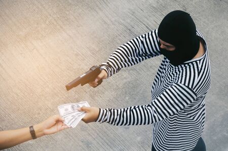 thief or robber in black and white jacket and masked hood with gun threatens man or woman fo steal money, dangerous criminal in the city, victim, violence, crime and steal conceptの写真素材