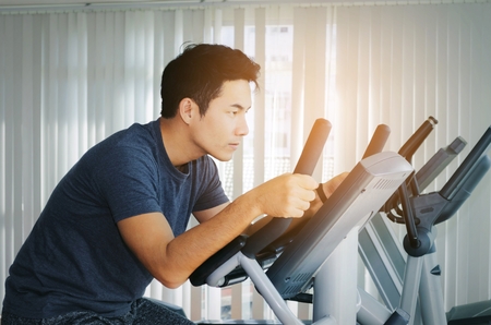 muscular young asian man exercising his legs cardio training on bicycle in fitness gym for good...