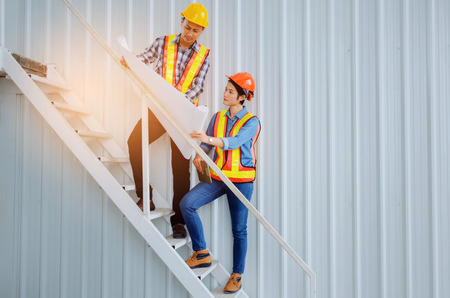couple of engineer or technician man and woman with safety helmet looking blueprint in construction...