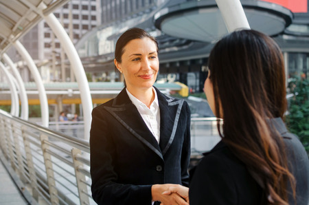 two business asian and caucasian woman handshake after finishing up a business meeting in the modern city, congratulation, success, meeting, partner, teamwork, community and connection conceptの写真素材