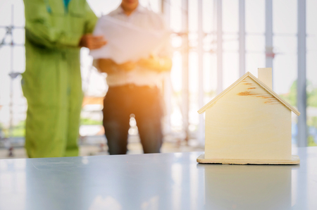 wooden house model with blurred view of technician, architect or engineer in background at construction site, planning start up new project, successful, industry, architecture, housing project conceptの写真素材