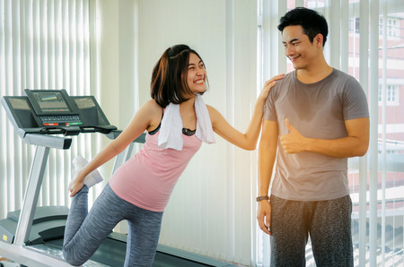 asian young smiling sport woman stretching in fitness gym center with personal trainer man showing thumbs up, bodybuilder, healthy lifestyle, exercise fitness, workout and sport training conceptの写真素材
