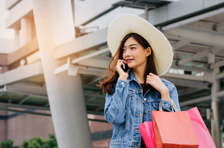 cheerful asian young woman making phone call on mobile smart phone with shopping bags in big city, black friday, technology, internet, winter sale, promotion, payment and shopping online conceptの写真素材