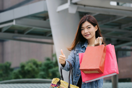 beautiful cheerful asian young woman holding many colorful shopping bags and walking in modern city, winter sale, black friday, promotion, special offer sale, shopping and payment online conceptの写真素材