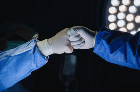 Doctor and Assistant surgeon joining hands together after work for rescue patient in operation room at hospital, emergency case, surgery, medical technology, cancer and disease treatment conceptの写真素材