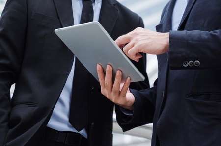 midsection two business asian smart man talking and reading information about finance news in mobile tablet together standing in modern city, network technology, internet, successful, teamwork conceptの写真素材
