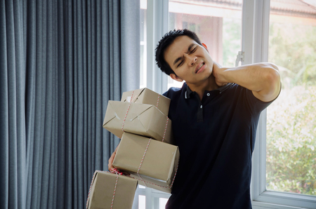 handsome young asian delivery man lifting many heavy packaging parcel box and be tired in home office, small business owner, cargo, mail, transportation, shopping online and shipping conceptの写真素材