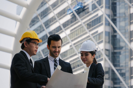 group of business or engineer woman and man with safety helmet and blueprint planning at the building and checking their work in modern city, planning start up new project, successful conceptの写真素材