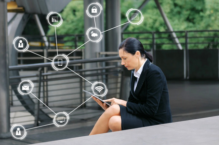 caucasian business woman wearing modern black suit reading information about finance news with mobile tablet in city with icon network, investment, technology, internet, successful conceptの写真素材