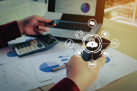 young man entering security code with smart phone and paying with credit card and laptop computer on desk at home office with graphic icon diagram, payment and shopping online, technology conceptの写真素材