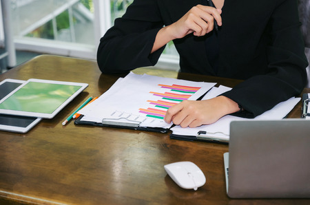young business woman in black suit sitting and working with tablet, laptop and document chart on desk in office, investment, financial, technology, company success and business growth conceptの写真素材