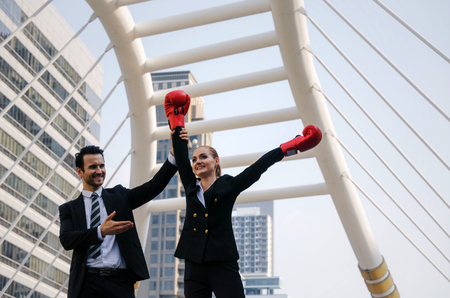 handsome business man raising his business woman partners hand with boxing gloves in modern city, celebrating, winner gesture, team leader, successful, support, teamwork, community, confident conceptの写真素材