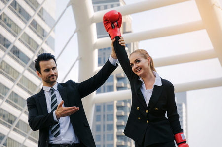 handsome business man raising his business woman partners hand with boxing gloves in modern city, celebrating, winner gesture, team leader, successful, support, teamwork, community, confident conceptの写真素材